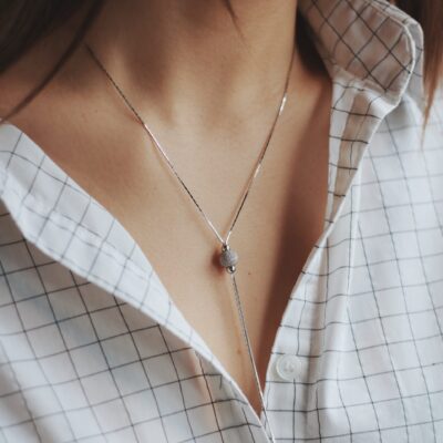 A closeup shot of a female wearing a white shirt and a delicate silver charm necklace